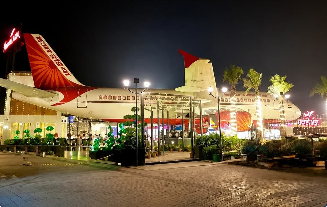 The Hawai Adda aircraft restaurant in Amritsar at night: an Air India liveried airliner beside a glass enclosure and palm trees