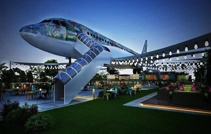 Terminal C - Jurassic Park: an aircraft restaurant in Sonipat with a graffiti-wrapped fuselage, spiral stairs and string lights at dusk