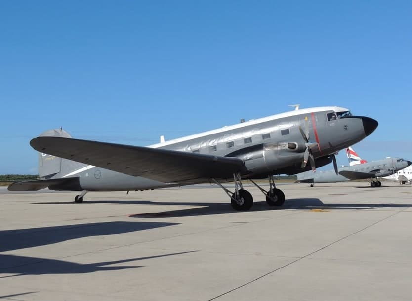 A polished-aluminium Douglas DC-3 Dakota parked on an airfield apron