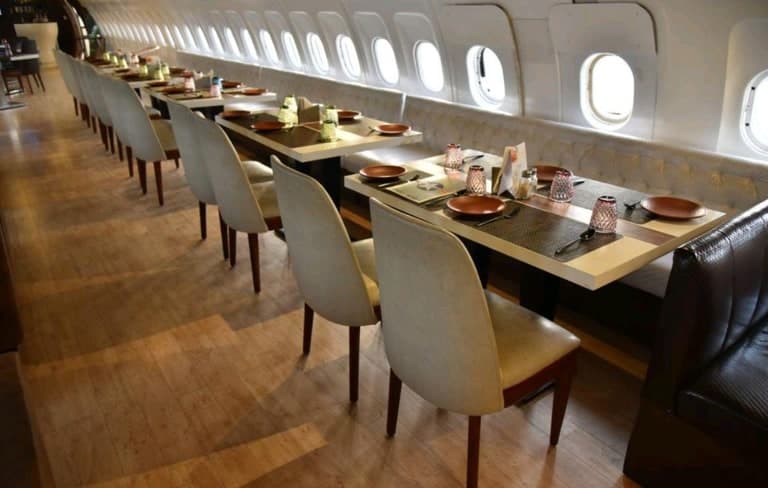 An aircraft cabin converted into a dining room, with a long table set for guests along the windows