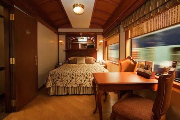 A luxury train bedroom cabin with wood panelling, a bed and a desk